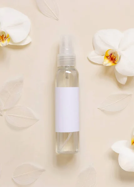 One pump dispenser bottle near white orchid flowers on light yellow top view, mockup. Skincare beauty product package. Exotic natural cosmetics, pastel minimal compositio