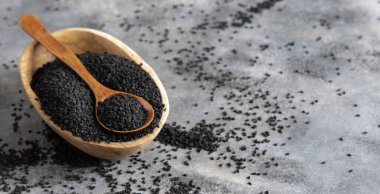 Hint baharatlı kimyon (nigella sativa veya kalonji) tohumları kasede, gri masada kaşıkla fotokopi alanı ile yakın çekim yapar. Geleneksel tıp, sağlıklı ve vejetaryen gıda konsepti.