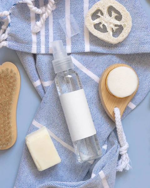 Refillable Spray bottle, skin and hair care accessories on blue bath towel near tropical leaves top view, copy space. Packaging mockup. Natural homemade products