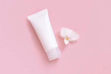 Beyaz orkide çiçeğinin yanında beyaz plastik krema tüpü açık sarı, üst manzara, model. Cilt bakım ürünü, krem ya da losyon. Egzotik doğal kozmetik ürünler, pastel minimum bileşik.