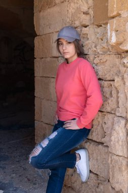 Pembe uzun kollu gömlek giyen ve beyzbol şapkası takan genç kız yan bakıyor. Modelleme. Ciddi bir ergen kız dışarıda, duvarın yanında duruyor ve zamanını yalnız geçiriyor. Ergenlik konsepti
