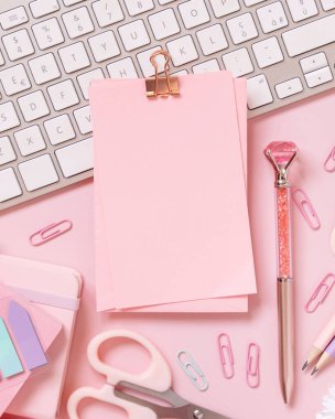 Şarjörlü kağıt, pembe okul aksesuarları ve açık pembe klavye, üst manzara, maket. Not defteri, makas, kalem, ataç ve kartı olan kız işyeri. Okula geri dön. 