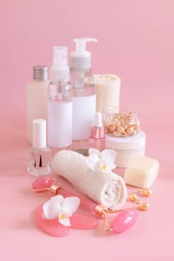 Natural cosmetic jars, skin care accesories and rose quartz face massagers with white orchid flower on light pink close up. Beauty products mockup. Everyday woman face care routine, Spa Treatments