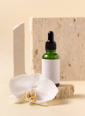 Beyaz orkide çiçeğinin yanında taşın üzerinde yeşil cam damlatan şişe açık sarıda, yakın plan, maket. Cilt bakımı el yapımı güzellik ürünü, serum veya losyon. Egzotik doğal kozmetik