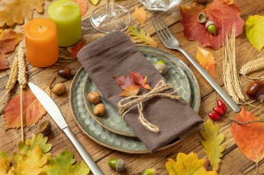 Autumn rustic table setting between leaves and berries on vintage wooden table close up. Thanksgiving, halloween or harvest concept