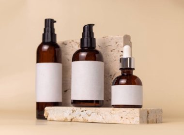 Brown glass one pump bottles on travertine stones on light beige close up, label mockup. Skincare beauty product package. Natural cosmetics, minimal compositio