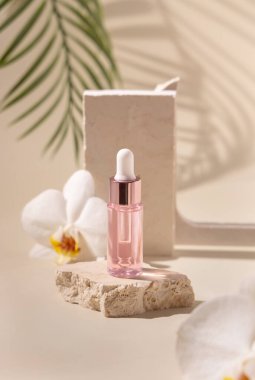 Dropper Bottle on stone near white orchid flowers and palm leaves on light yellow, close up, mockup. Skincare beauty product, essential oil or serum. Exotic cosmetics, pastel minimal compositio