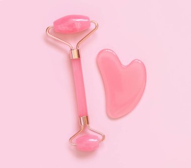 Pink quartz Facial roller and gua sha massager on light pink top view. Anti-age massage and natural lifting therapy. Facial skin care at home. Beauty concept. Monochrome flat lay