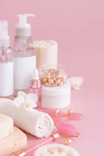 Natural cosmetic jars, skin care accesories and rose quartz face massagers with white orchid flower on light pink close up. Beauty products mockup. Everyday woman face care routine, Spa Treatments