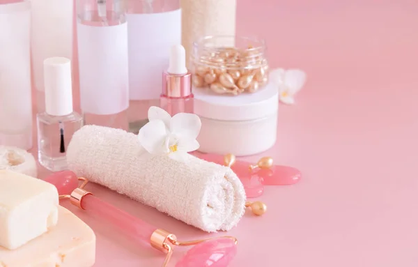 Natural cosmetic jars, skin care accesories and rose quartz face massagers with white orchid flower on light pink close up. Beauty products mockup. Everyday woman face care routine, Spa Treatments