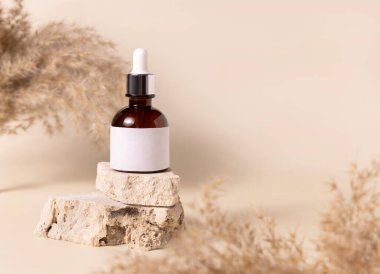 Brown dropper bottle with blank label on travertine stone near dry pampas grass on light yellow, close up, mockup. Skincare beauty product. Natural cosmetics. Boho compositio