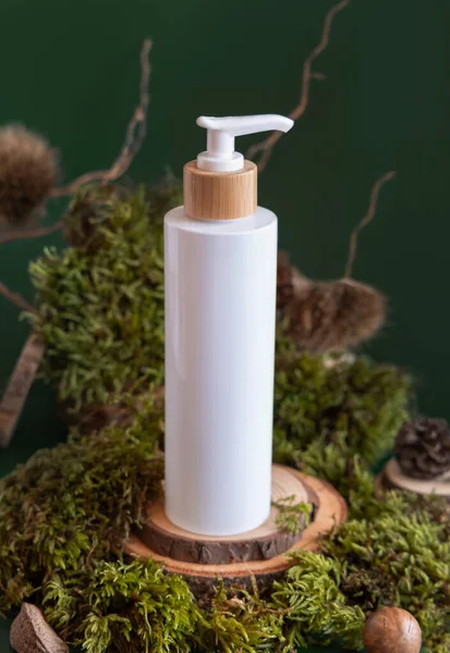 White Refillable Cosmetic Pump Dispenser on wooden piece between green moss, close up, mockup. Skincare beauty product package. Natural Organic Cosmetic concept