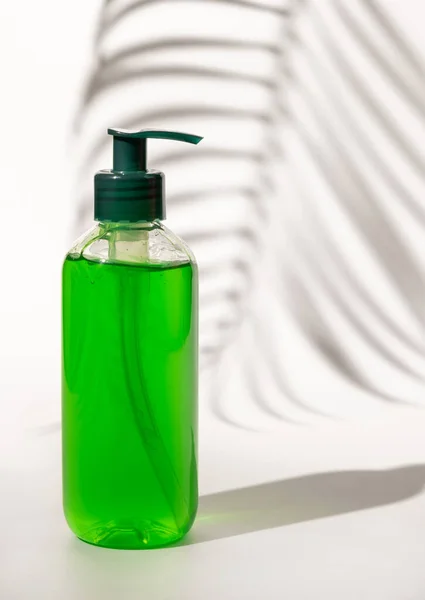 Refillable Cosmetic pump dispenser bottle filled with green liquid on white, Palm leaf hard shadows, close up, mockup. Skincare beauty product, facial cleaner or lotion. Natural cosmetic