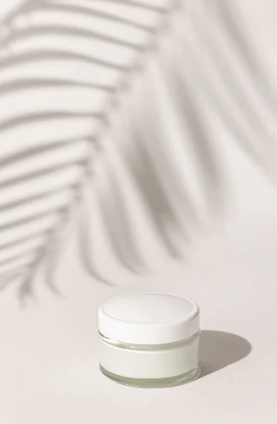 Cream jar with a blank white lid on white close up, Palm leaf hard shadow. Cosmetic packaging Mockup. Exotic natural cosmetics, monochrome composition, everyday skincare routin