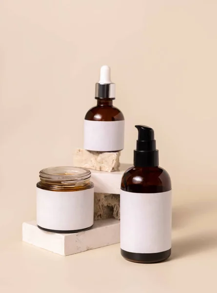 Cosmetic bottles on beige stones on light beige close up. Labels Mockup. Skincare beauty product packages. Natural cosmetics, minimal boho compositio