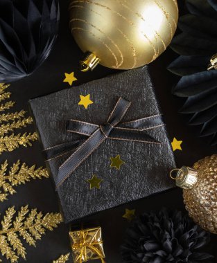 Christmas Gift Box with a bow near black and golden ornaments and baubles top view. Dark winter flat lay for Christmas, New Year, Birthday, Anniversary 