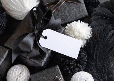 Gift Boxes with Black and white paper flowers and decorations, horizontal gift tag Mockup, copy space. Dark composition with blank label card for Christmas, New Year, Birthday, Anniversary 