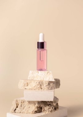 Pink glass cosmetic dropper bottle on beige travertine stones on light yellow close up, mockup. Skincare natural beauty product. Minimal eco friendly compositio