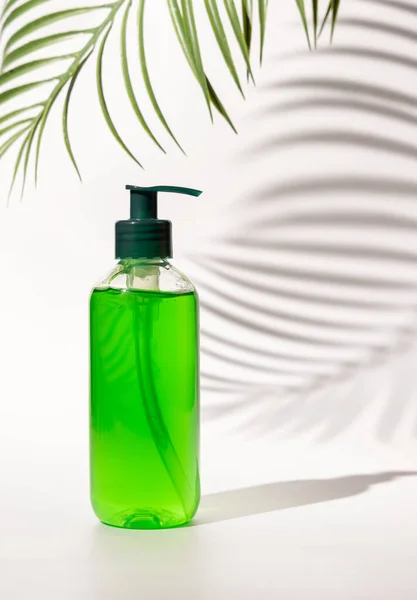 Refillable Cosmetic pump dispenser bottle filled with green liquid on white, Palm leaf hard shadows, close up, mockup. Skincare beauty product, facial cleaner or lotion. Natural cosmetic