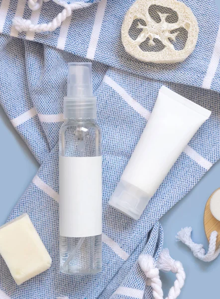 Cosmetic pump dispenser bottle and white cream tube on blue bath towel top view, copy space. Packaging mockup. Natural homemade products
