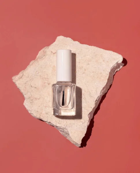 Clear Glass Refillable Bottle with Brush Cap near beige travertine stones on pink, top view, mockup. Hard shadow. Skincare nail product. Natural cosmetics, minimal compositio