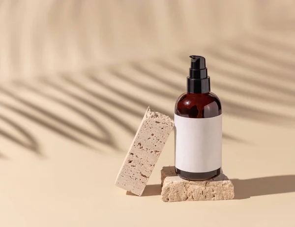 Brown Glass cosmetic one pump bottle on travertine stone on light beige. Palm leaf hard shadows, close up, label mockup. Skincare beauty product, lotion or essence. Natural cosmetic