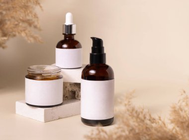 Cosmetic bottles on beige stones near dry pampas grass on light beige close up. Labels Mockup. Skincare beauty product packages. Natural cosmetics, minimal boho compositio