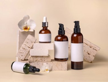 Dark glass bottles with blank labels near white orchid flowers and stones on light beige, close up, package mockup. Skincare beauty products, serum, tonic or lotion. Exotic natural cosmetics