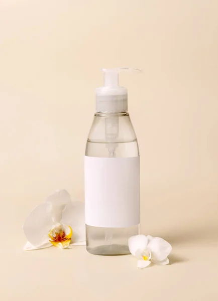 Cosmetic pump dispenser bottle near white orchid flowers on light beige close up, mockup. Skincare beauty product package. Exotic natural cosmetics, pastel minimal compositio