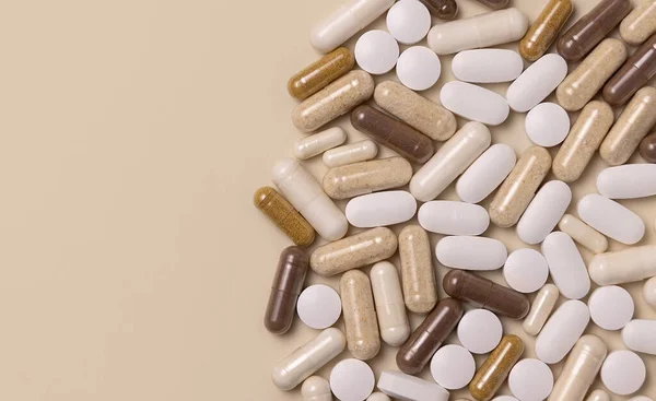 Mix of medical capsules and pills on light beige top view, copy space. Preventive medicine and healthcare, taking dietary supplements and vitamins.  Assorted pharmaceutical medicine capsules