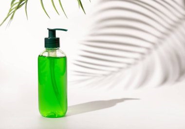 Refillable Cosmetic pump dispenser bottle filled with green liquid on white, Palm leaf hard shadows, close up, mockup. Skincare beauty product, facial cleaner or lotion. Natural cosmetic