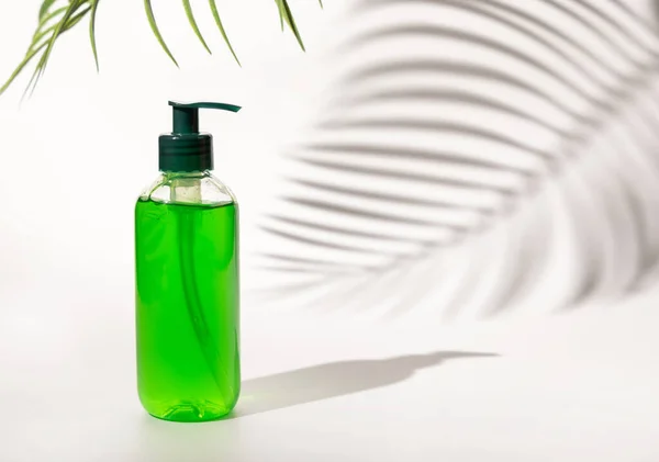 Refillable Cosmetic pump dispenser bottle filled with green liquid on white, Palm leaf hard shadows, close up, mockup. Skincare beauty product, facial cleaner or lotion. Natural cosmetic