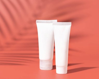 Two white blank plastic tubes on pink close up, palm leaf hard shadows, mockup. Skincare beauty product, body lotion or cream. Natural cosmetic