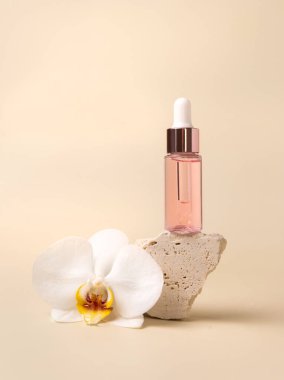 Dropper Bottle on stone near white orchid flowers on light yellow, close up, mockup. Skincare beauty product, essential oil or serum. Exotic cosmetics, pastel minimal compositio