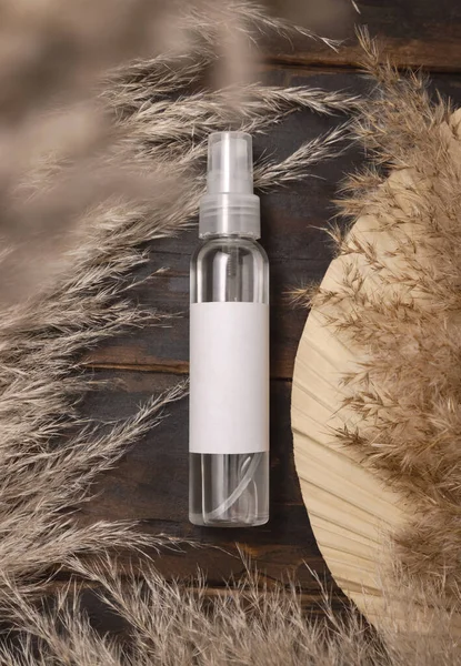 Transparent spray bottle on wood near dried palm leaf and pampas grass top view, label mockup. Skincare beauty product, cleanser or water. Bohemian eco friendly cosmetics flat lay with dried leave
