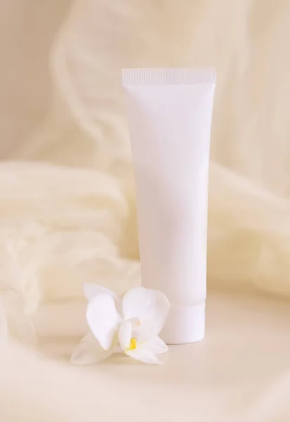 White Cream tube near orchid flowers and tulle on light beige close up. Packaging Mockup. Exotic natural cosmetics, romantic composition, everyday skincare routin
