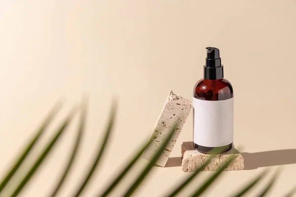 Glass cosmetic one pump bottle on stone on light beige with a palm leaf, close up, label mockup. Skincare beauty product, lotion or essence. Natural cosmetic