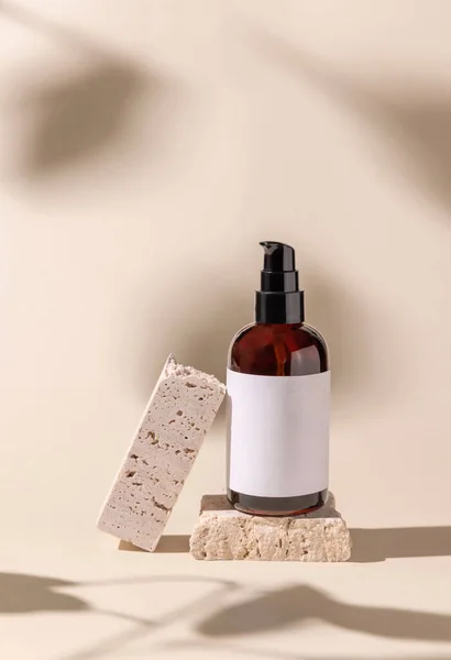 Brown Glass cosmetic one pump bottle on travertine stone on light beige, hard shadows, close up, label mockup. Skincare beauty product, lotion or essence. Natural cosmetic