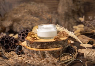 Opened glass cream jar on wood near natural decorations close up, package mockup. Eco friendly skincare product, lotion or cream. Bohemian composition with dried leaves and flower