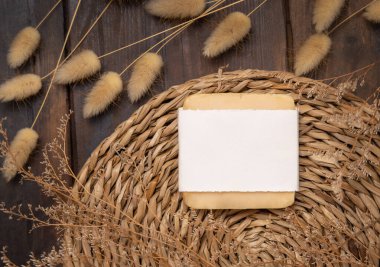 Soap bar with blank label on wattled placemat on wood near Hare's Tail grass top view, packaging mockup. Natural handmade skincare product. Bohemian eco friendly flat la