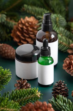 Köknar dallarının yanında kahverengi cam kavanozlar ve koyu yeşil üzerinde çam kozalakları. Marka ambalaj modeli. Cilt bakım ürünü, krem ya da serum. Sağlık hizmetleri doğal kozmetik konsepti