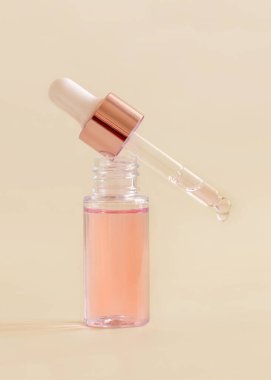 Opened Bottle with serum drop falling from pipette cap on light beige, close up, copy space. Skincare cosmetic product, essence or serum. Everyday beauty routin