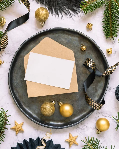 Black and golden Table setting with ornaments and fir tree branches top view, invitation card mockup. Christmas or New Year atmospheric composition on marble table, copy space.