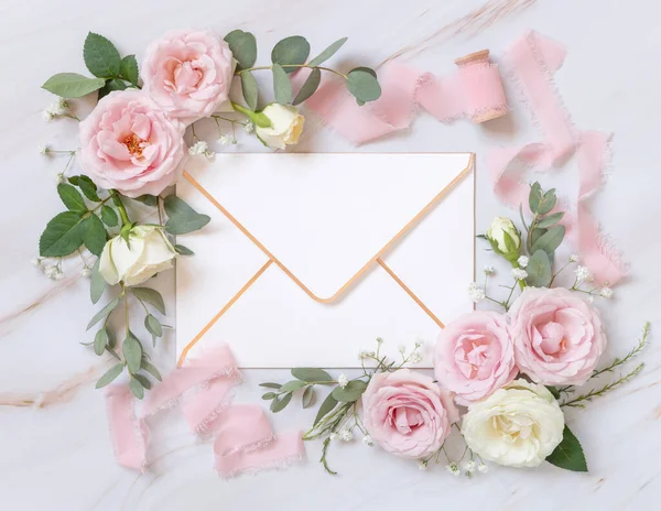 在浅粉玫瑰和丝带之间的纸制信封在大理石顶视图上 婚纱造型 浪漫的场景 用空白的信封和柔和的花朵平铺着 情人节 春天或母亲节 — 图库照片