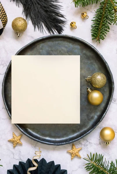 Black and golden Table setting with ornaments and fir tree branches top view, square card mockup. Christmas or New Year atmospheric composition on marble table, copy space.