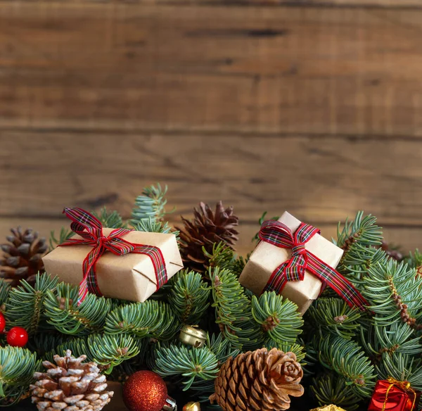 クリスマスの装飾の近くの赤いモミの枝にギフトボックスを包み 木製の背景に松のコーンを閉じ スペースをコピーします クリスマスや新年の休日の雰囲気 — ストック写真