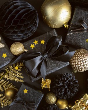 Christmas Gift Box with a bow near black and golden ornaments and baubles top view. Dark winter flat lay for Christmas, New Year, Birthday, Anniversary 