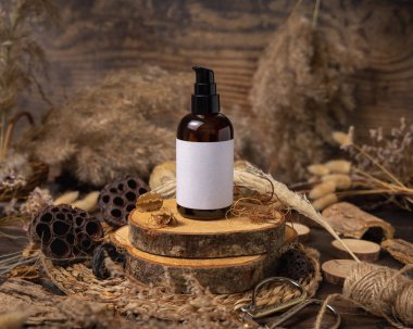 Glass one pump bottle on wood near natural boho decorations close up, label mockup. Skincare beauty product, lotion or essence. Bohemian eco friendly cosmetics flat lay with dried leave