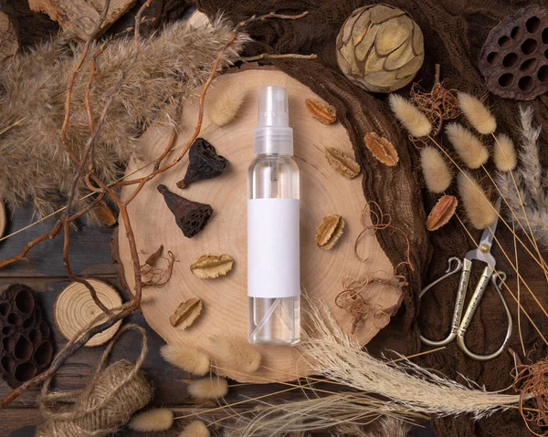 Transparent Refillable spray bottle on wood near natural boho decorations top view, label mockup. Skincare beauty product, lotion or essence. Bohemian eco friendly cosmetics flat lay with dried leave