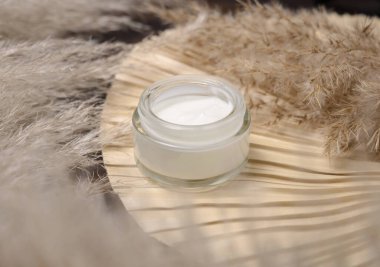 Pampa otlarının yanında kurutulmuş palmiye yaprağının üzerinde açılmış krema kavanozu yakın çekim, maket. Cilt bakım ürünü. Bohem çevre dostu kozmetik ürünleri kuru yapraklarla yatıyordu.